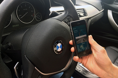 Hand hält Mobiltelefon vor Lenkrad im Auto