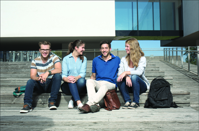 4 Personen sitzend im Innenhof der FH Oberösterreich Campus Hagenberg und in Kamera schauend